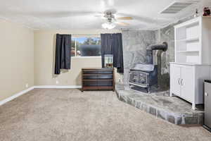 Family room featuring a wood stove, carpet floors, a ceiling fan, and a textured ceiling