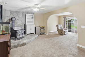 Living area featuring a wood stove, ceiling fan, light colored carpet, arched walkways, and a textured ceiling