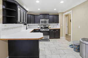 Kitchen featuring light countertops, backsplash, glass fronted cabinets, stainless steel appliances, and dark cabinetry