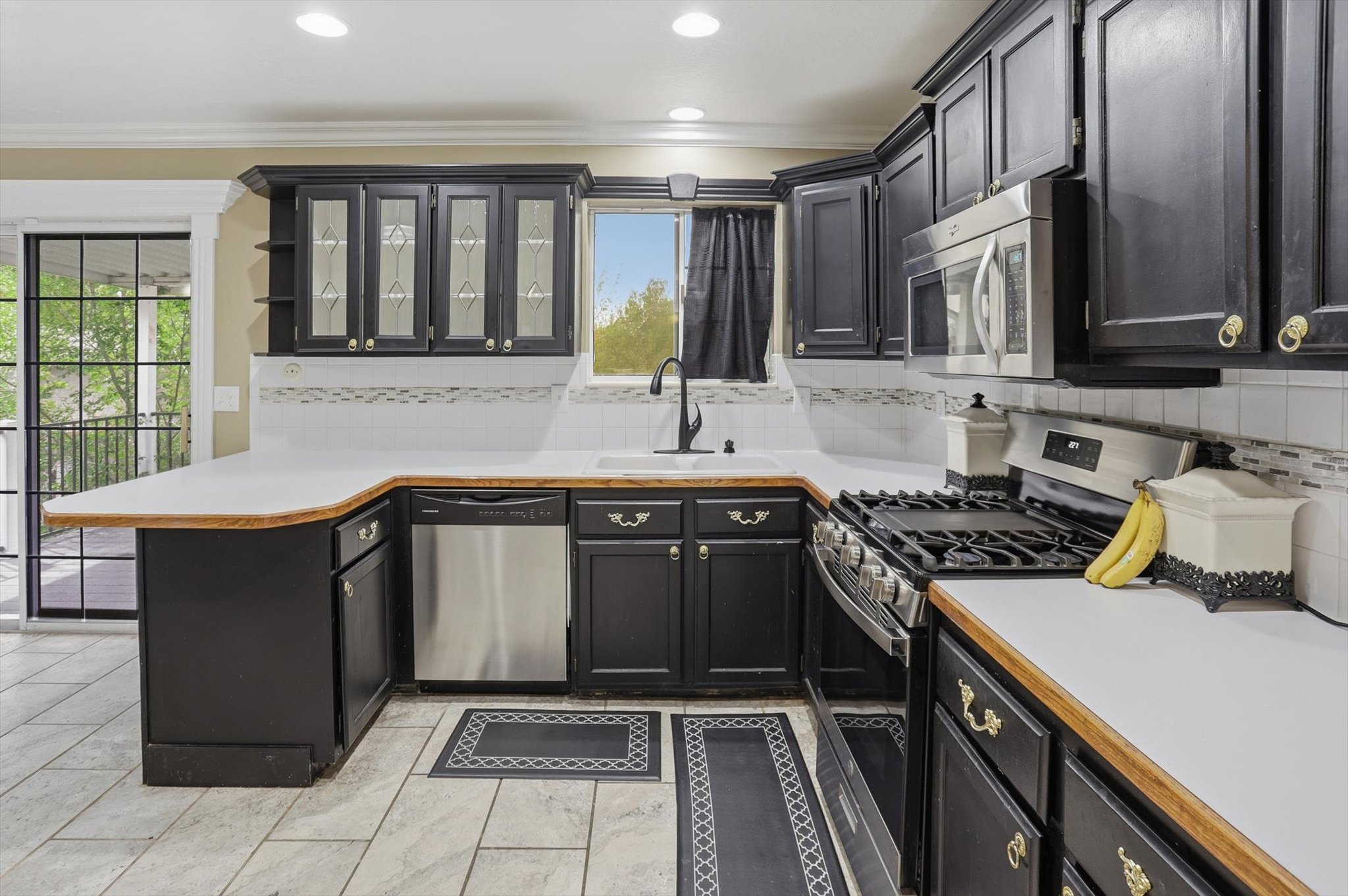 Kitchen featuring light countertops, stainless steel appliances, glass insert cabinets, decorative backsplash, and ornamental molding