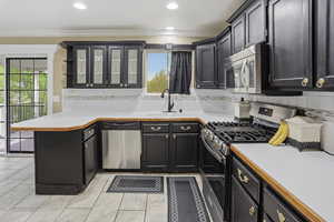 Kitchen featuring light countertops, stainless steel appliances, glass insert cabinets, decorative backsplash, and ornamental molding