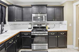 Kitchen featuring stainless steel appliances, light countertops, tasteful backsplash, dark cabinets, and light tile patterned flooring