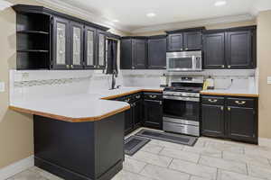 Kitchen featuring light countertops, stainless steel appliances, glass insert cabinets, dark cabinets, and tasteful backsplash