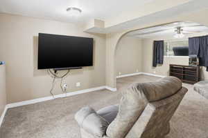 Living area featuring arched walkways, ceiling fan, light carpet, and a textured ceiling