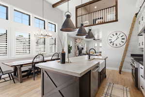 Dual tone kitchen with light wood-style floors, a center island with sink, stainless steel appliances, a high ceiling, and suspended lighting