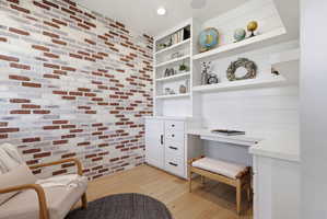 Sitting room with built in study area, light wood-type flooring, brick wall, and recessed lighting