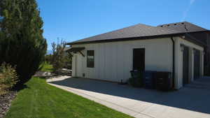 View of home's exterior with board and batten siding, a lawn, and a shingled roof