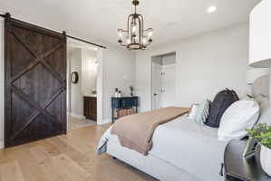 Bedroom with a barn door, light wood-style floors, a chandelier, and ensuite bathroom
