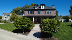 View of front of house with covered porch, brick siding, and a chimney