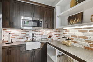 Kitchen with dark wood finish cabinetry, stainless steel microwave, tasteful backsplash, open shelves, and dark stone counters