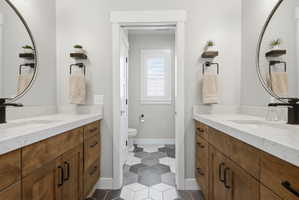Full bath with two vanities and dark tile patterned flooring