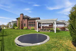 Rear view of house featuring a yard, a pergola, brick siding, and a chimney