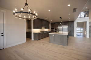 Kitchen featuring stainless steel appliances, an island with sink, light wood finished floors, suspended lighting, and decorative backsplash