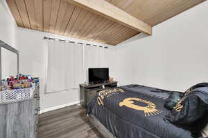 Bedroom with a wooden ceiling with exposed beams and dark wood-style floors