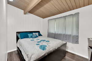 Bedroom with wood ceiling, dark wood-type flooring, wood walls, and lofted ceiling with beams