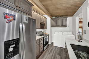 Kitchen featuring stainless steel appliances, dark wood finished floors, a vaulted wooden ceiling, and washing machine and clothes dryer