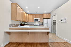 Kitchen featuring a peninsula, light countertops, white appliances, a kitchen breakfast bar, and recessed lighting