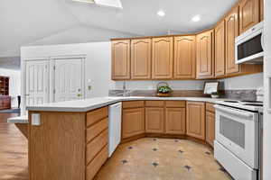 Kitchen with a peninsula, white appliances, light countertops, a skylight, and vaulted ceiling