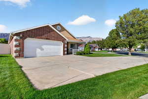 Ranch-style home featuring a mountain view, brick siding, concrete driveway, a garage, and a front lawn