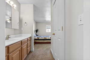 Bathroom with vanity, ensuite bath, a textured ceiling, and light colored carpet