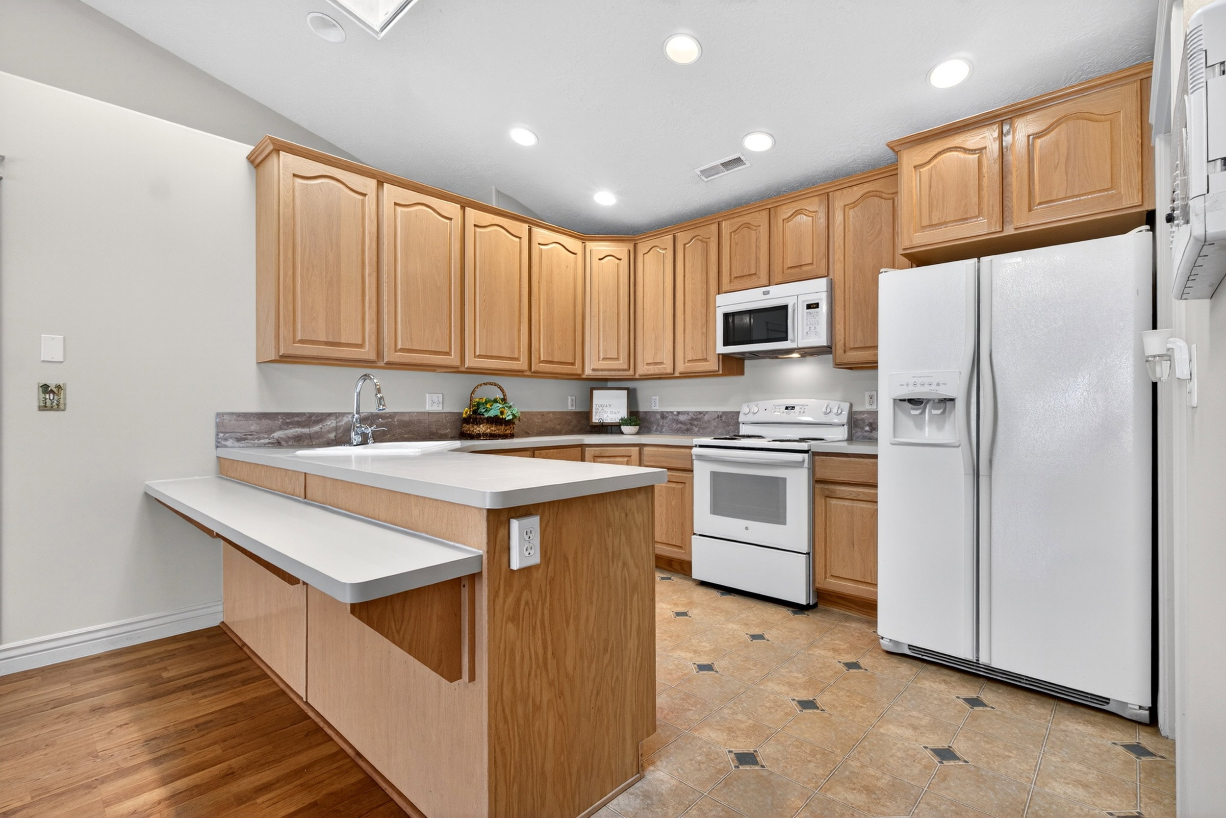 Kitchen featuring white appliances, a peninsula, light countertops, a breakfast bar area, and recessed lighting