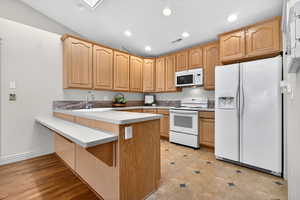 Kitchen featuring white appliances, a peninsula, light countertops, a breakfast bar area, and recessed lighting
