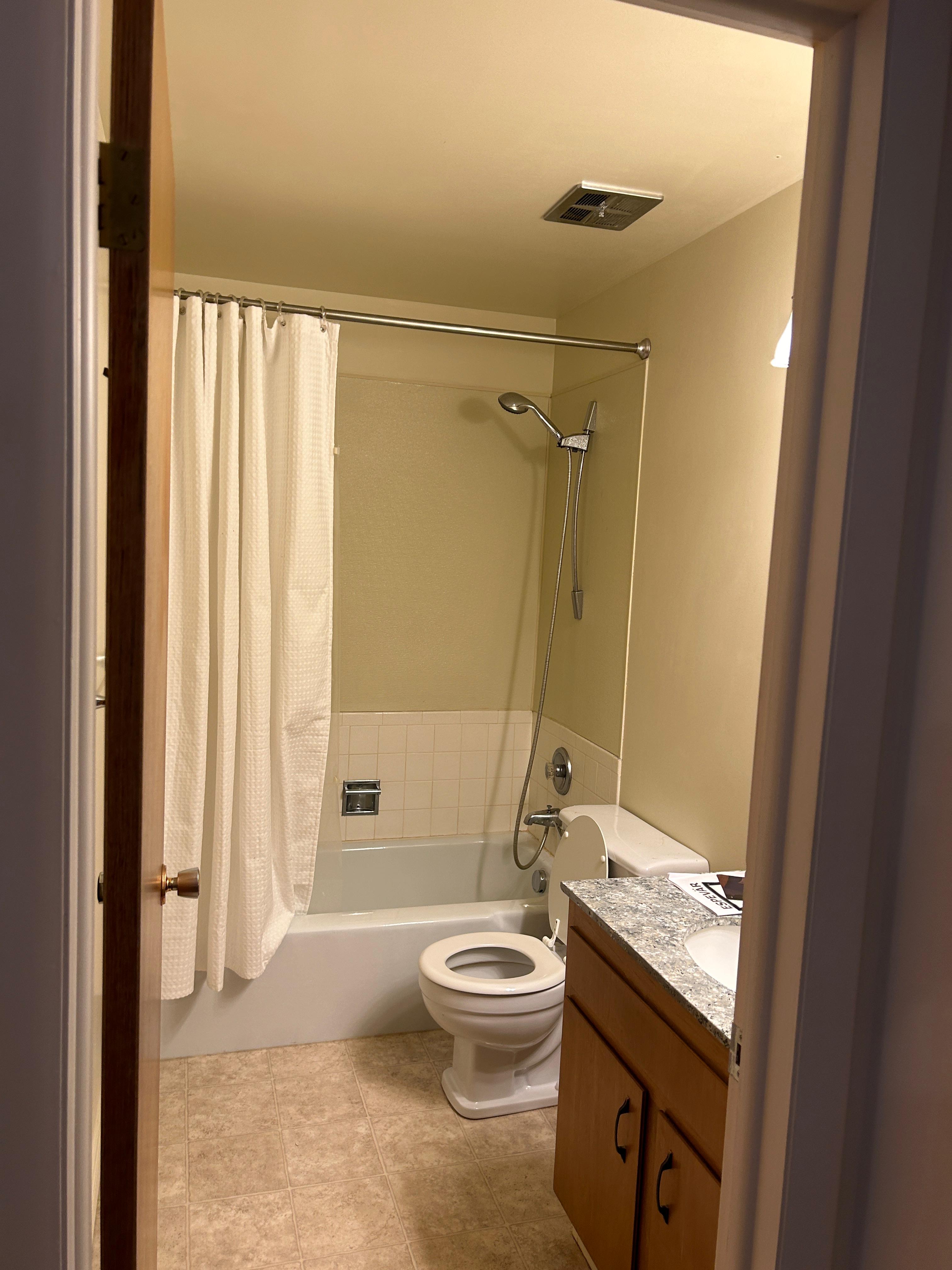 Bathroom featuring a tub/shower combination with tile surround, a single vanity with wood-finish cabinetry and a speckled countertop, and resilient flooring