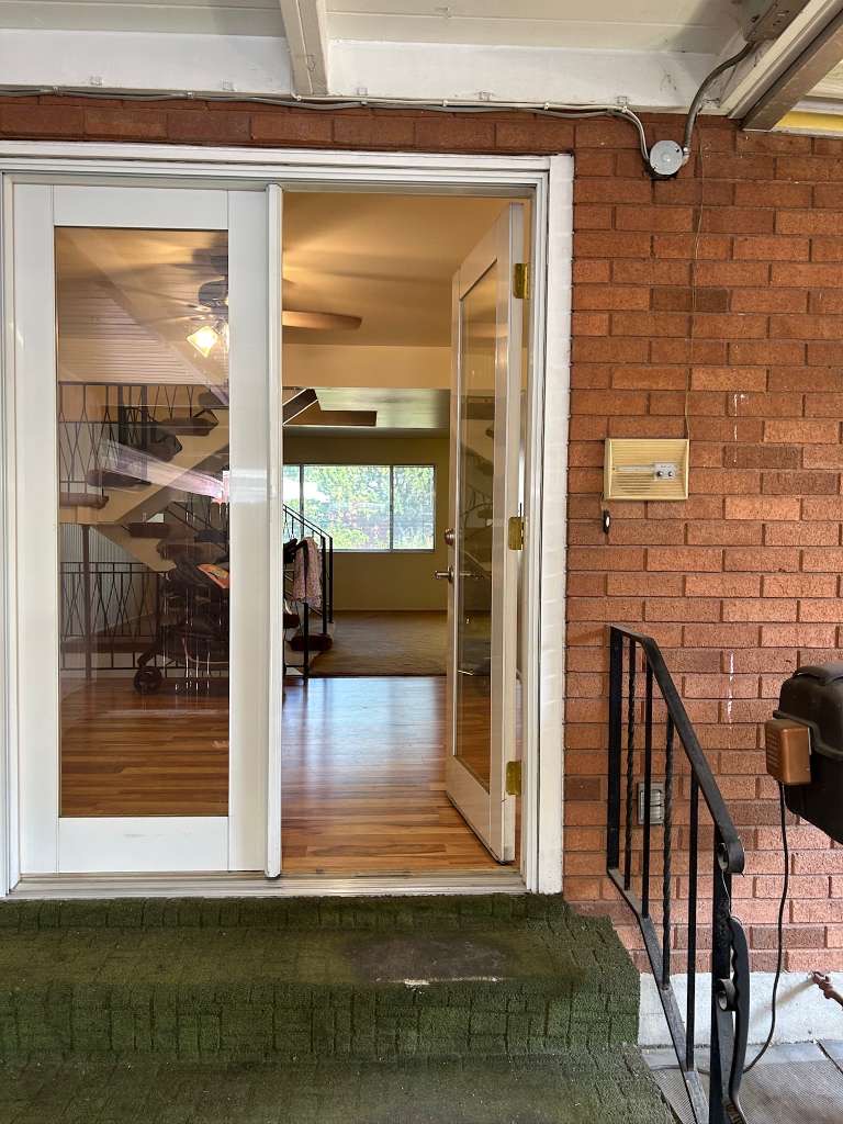 Exterior brick wall featuring glass-paneled double doors opening to an interior with wood-finish flooring