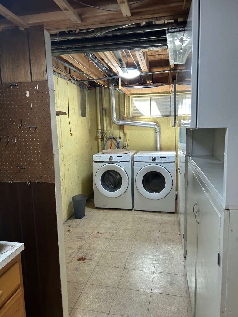 Laundry area featuring two front-loading machines, tiled flooring, built-in cabinetry, and exposed ceiling joists