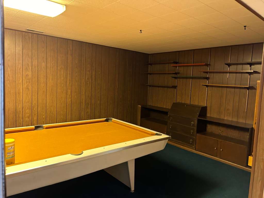 Recreation room featuring wood-panel walls, ceiling-mounted lighting, and built-in shelving with integrated cabinetry