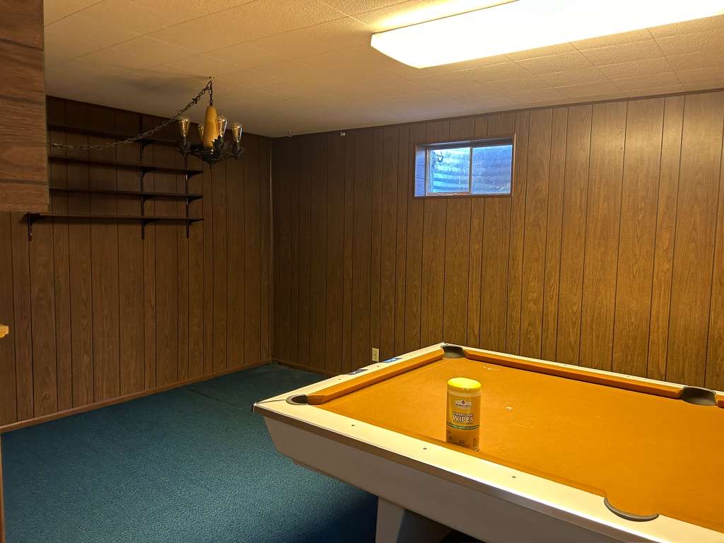 Room featuring wood-paneled walls, blue carpeting, and a drop ceiling with fluorescent lighting