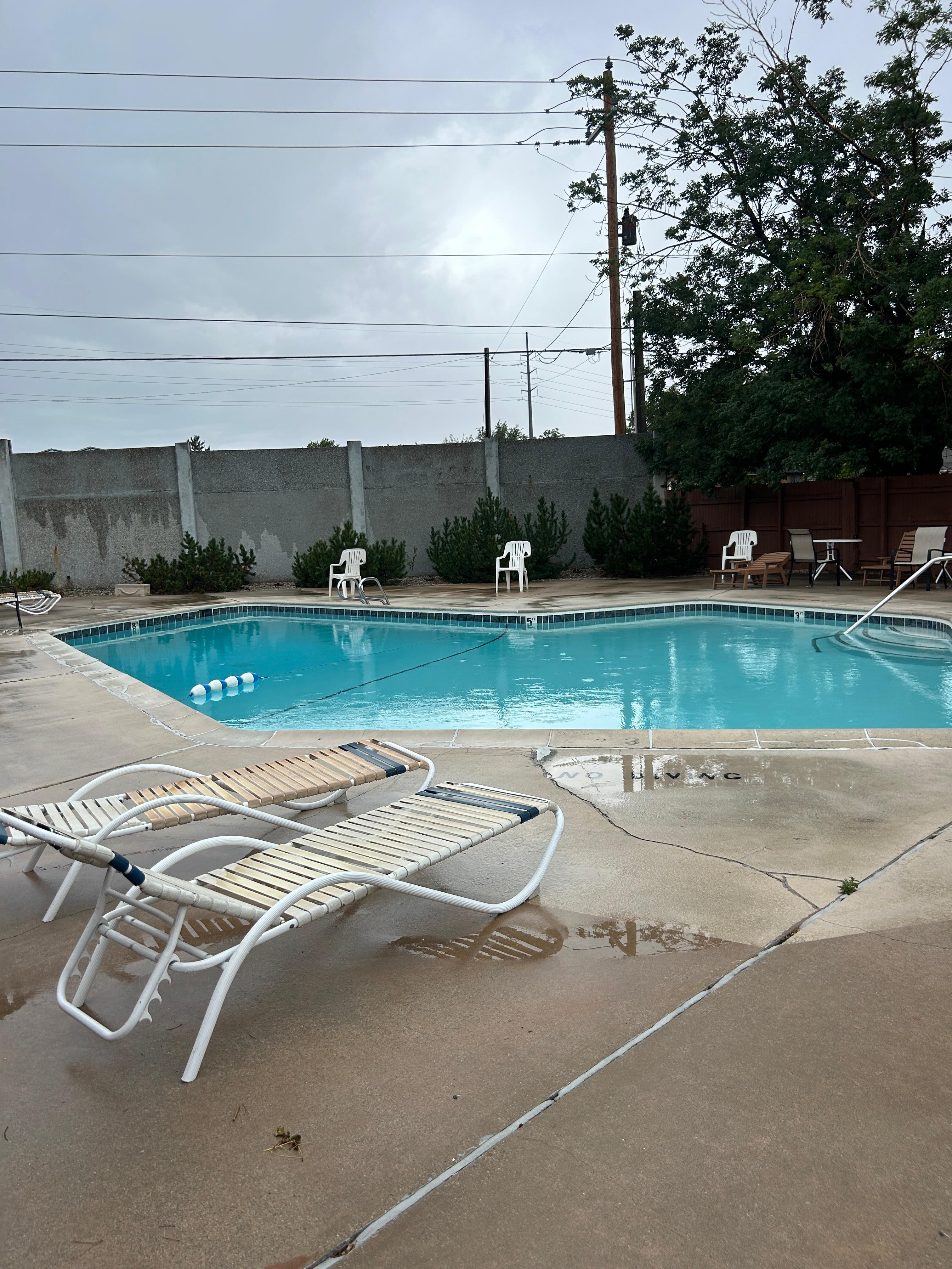 HOA Outdoor swimming pool with concrete surround, featuring a solid perimeter fence and mature landscaping