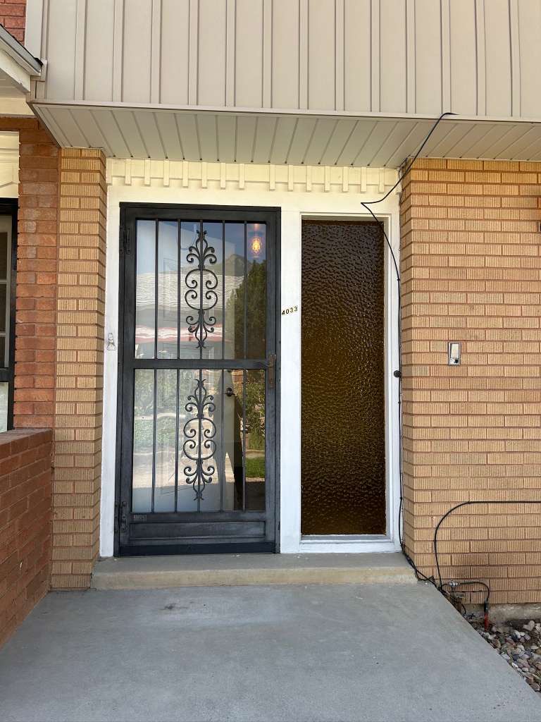 Brick exterior featuring a security screen door with decorative wrought ironwork, a textured glass entry door, and a covered concrete stoop