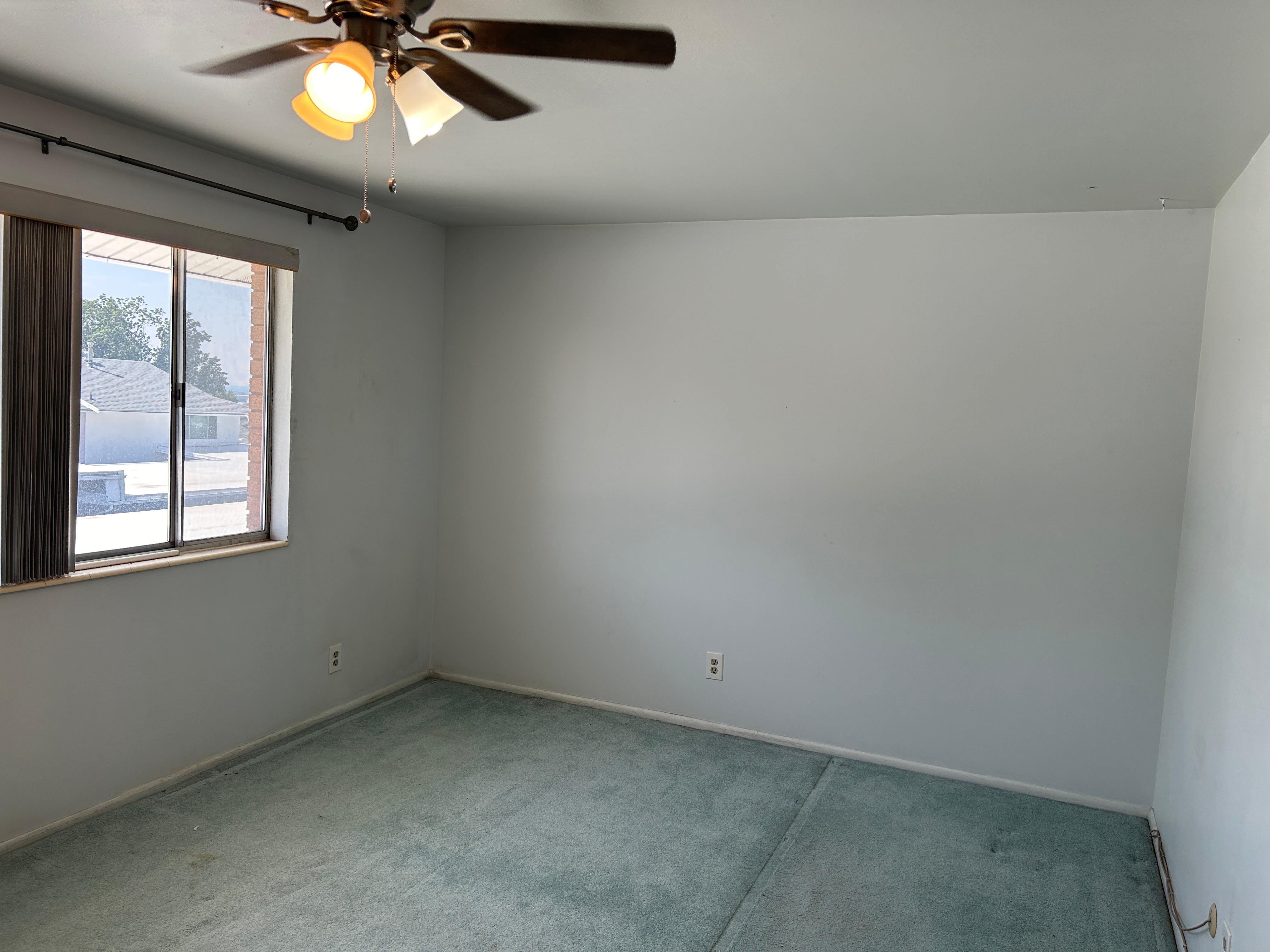 Bedroom featuring a ceiling fan with integrated lighting, a sliding window with vertical blinds, and wall-to-wall carpeting