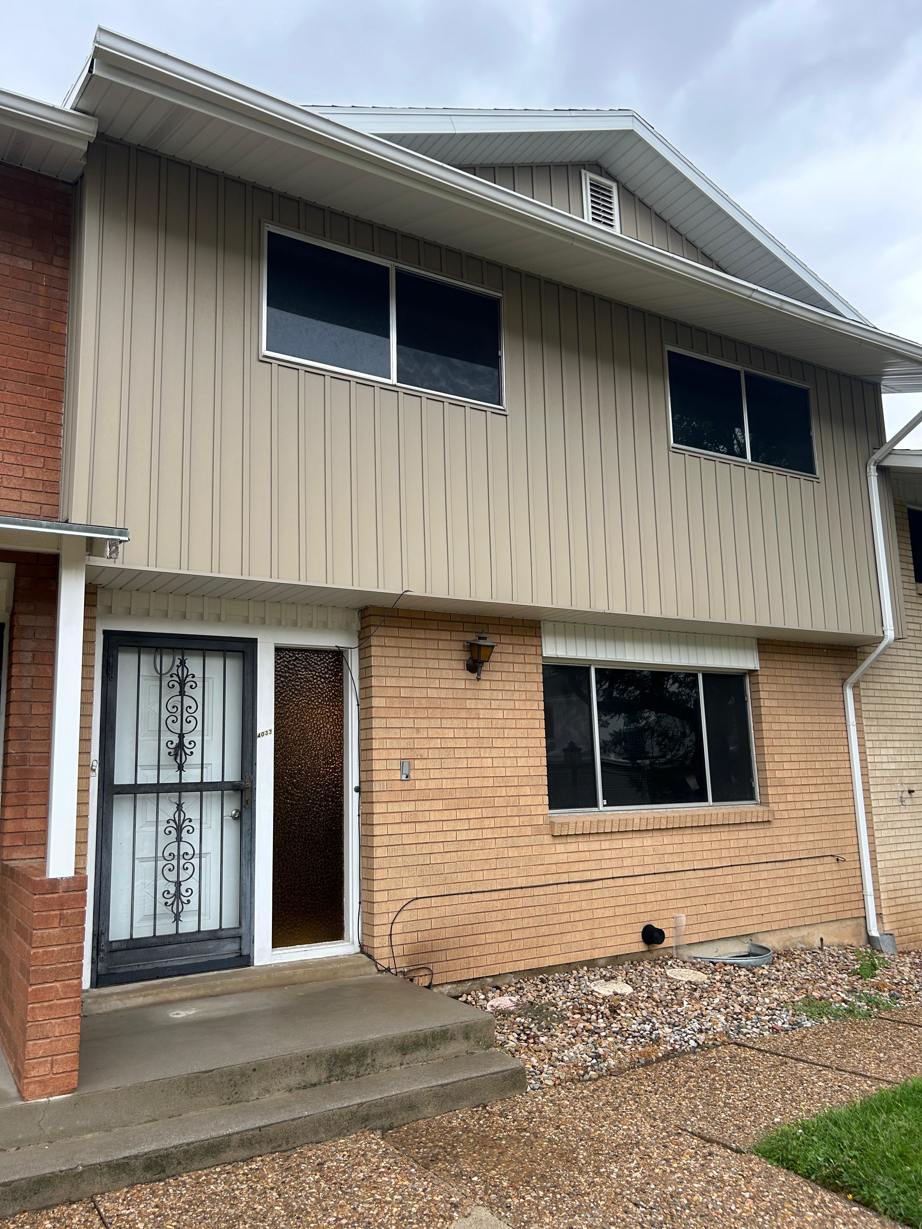 Two-story facade featuring tan vertical siding and brick accents