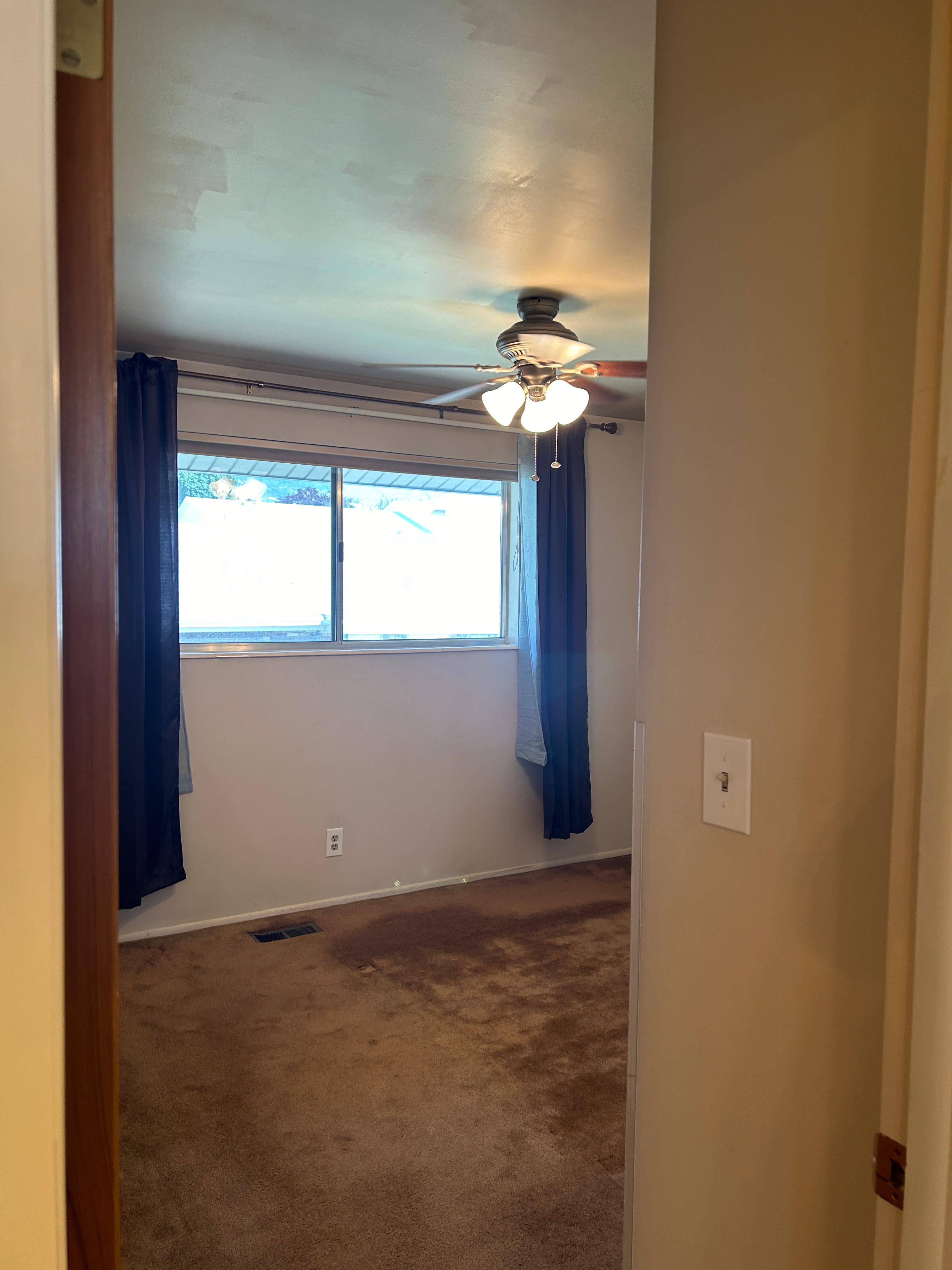 Room featuring a window with dark curtains, a ceiling fan with integrated lighting, and carpet flooring