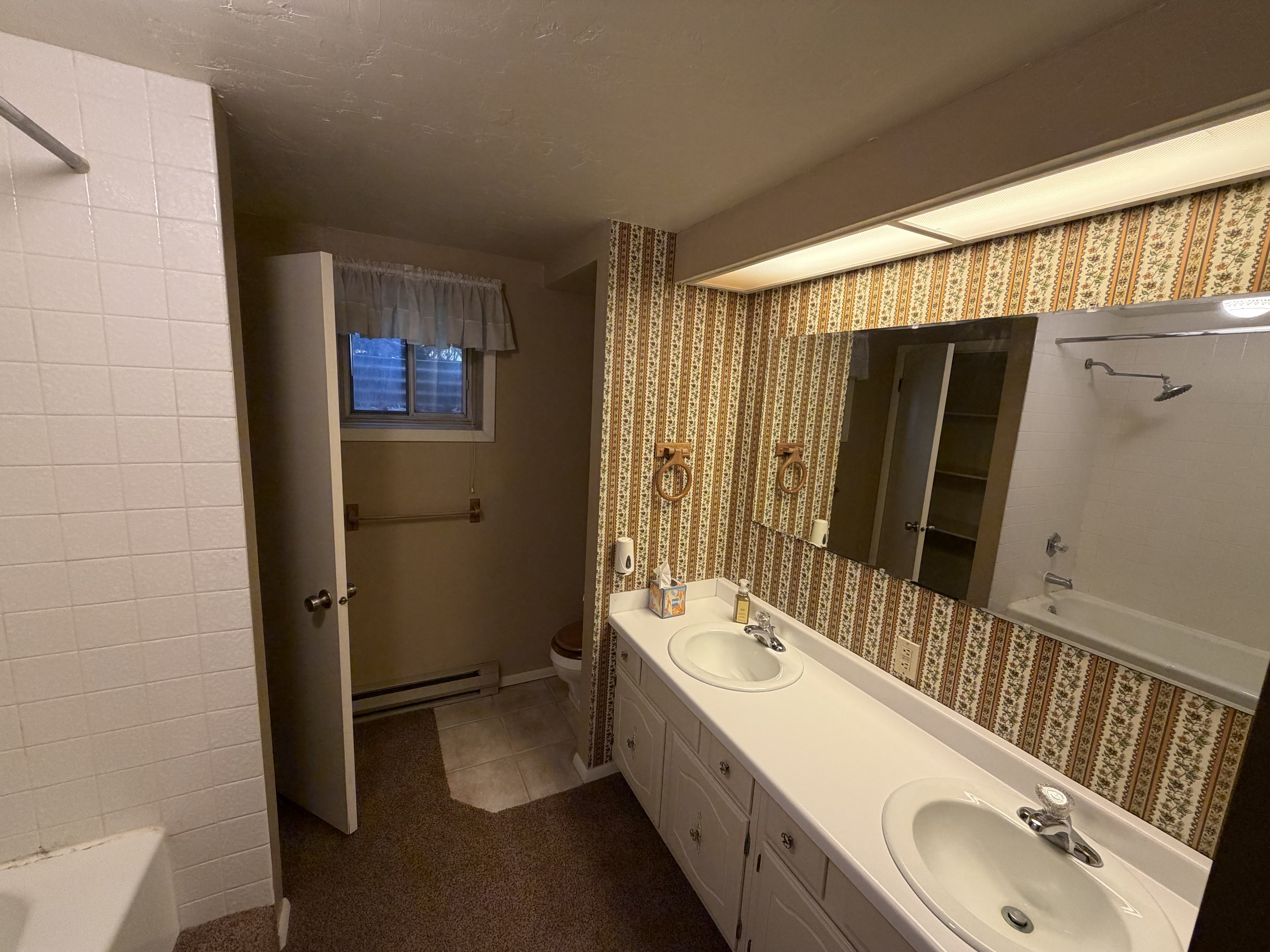 Bathroom with bathing tub / shower combination, double vanity, a baseboard radiator, dark tile patterned flooring, and wallpapered walls