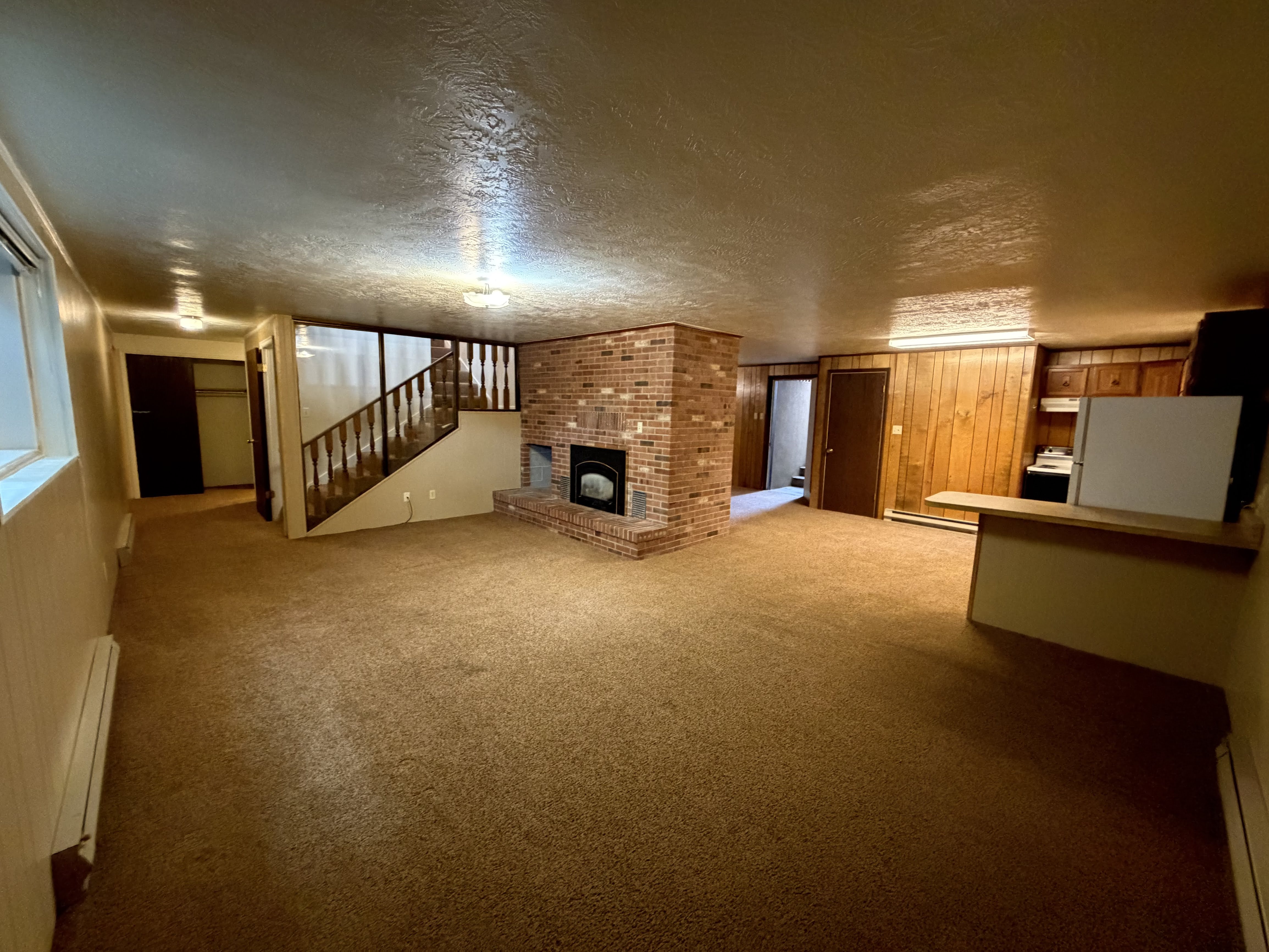 Unfurnished living room featuring a fireplace, a textured ceiling, light carpet, a baseboard radiator, and a baseboard heating unit