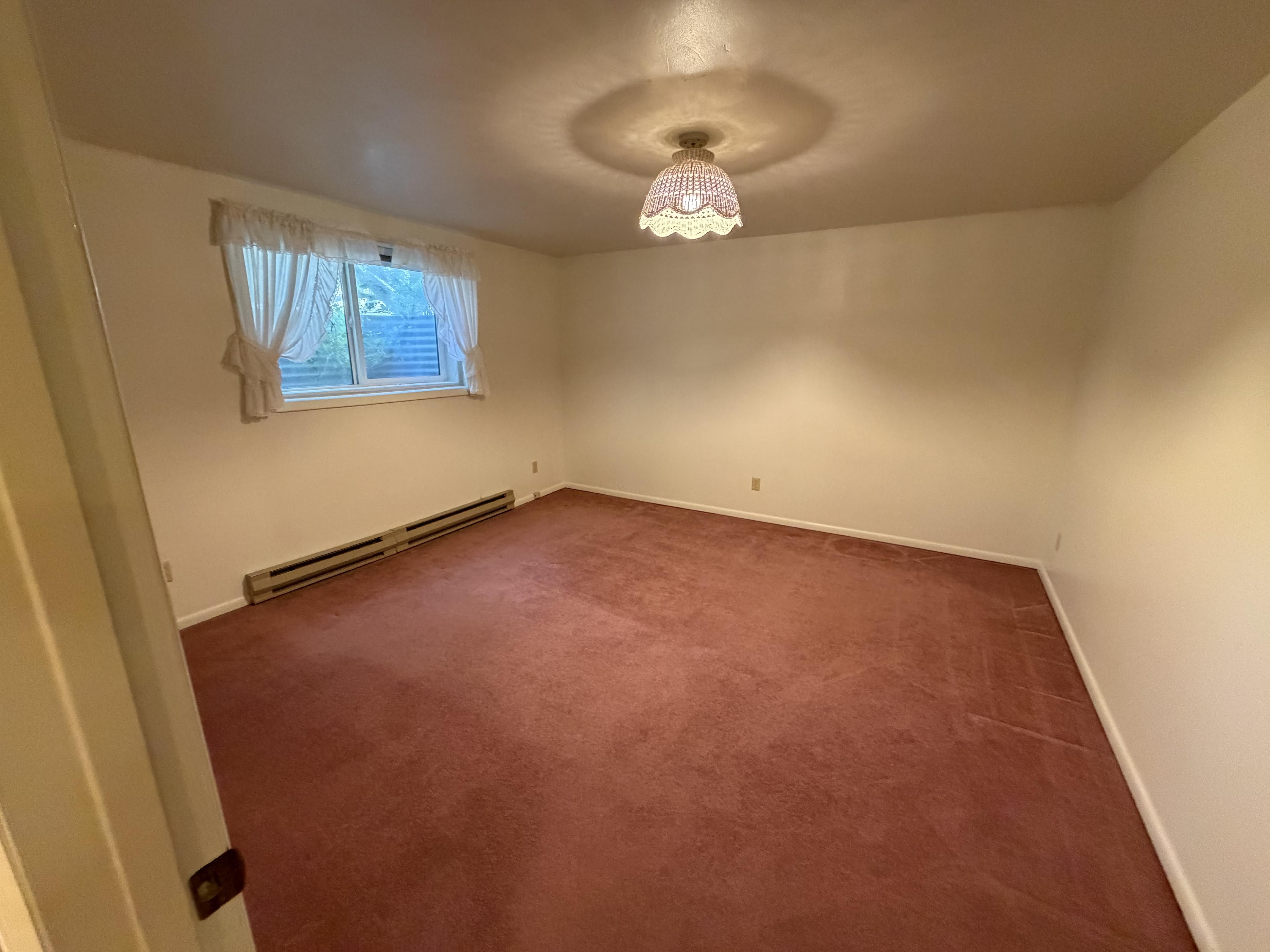 Carpeted empty room featuring a baseboard heating unit and baseboards