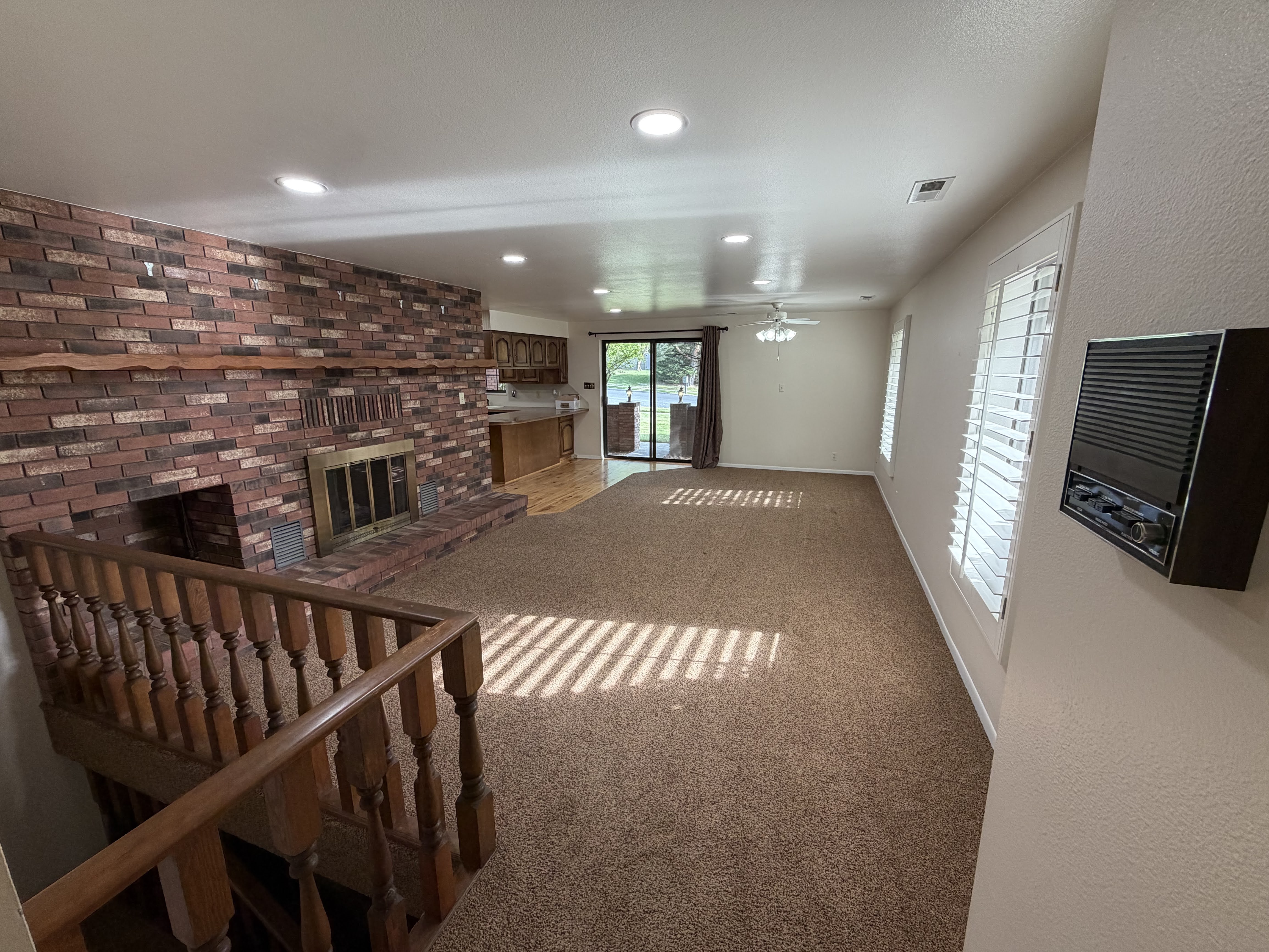 Unfurnished living room featuring a fireplace, light colored carpet, brick wall, recessed lighting, and a ceiling fan