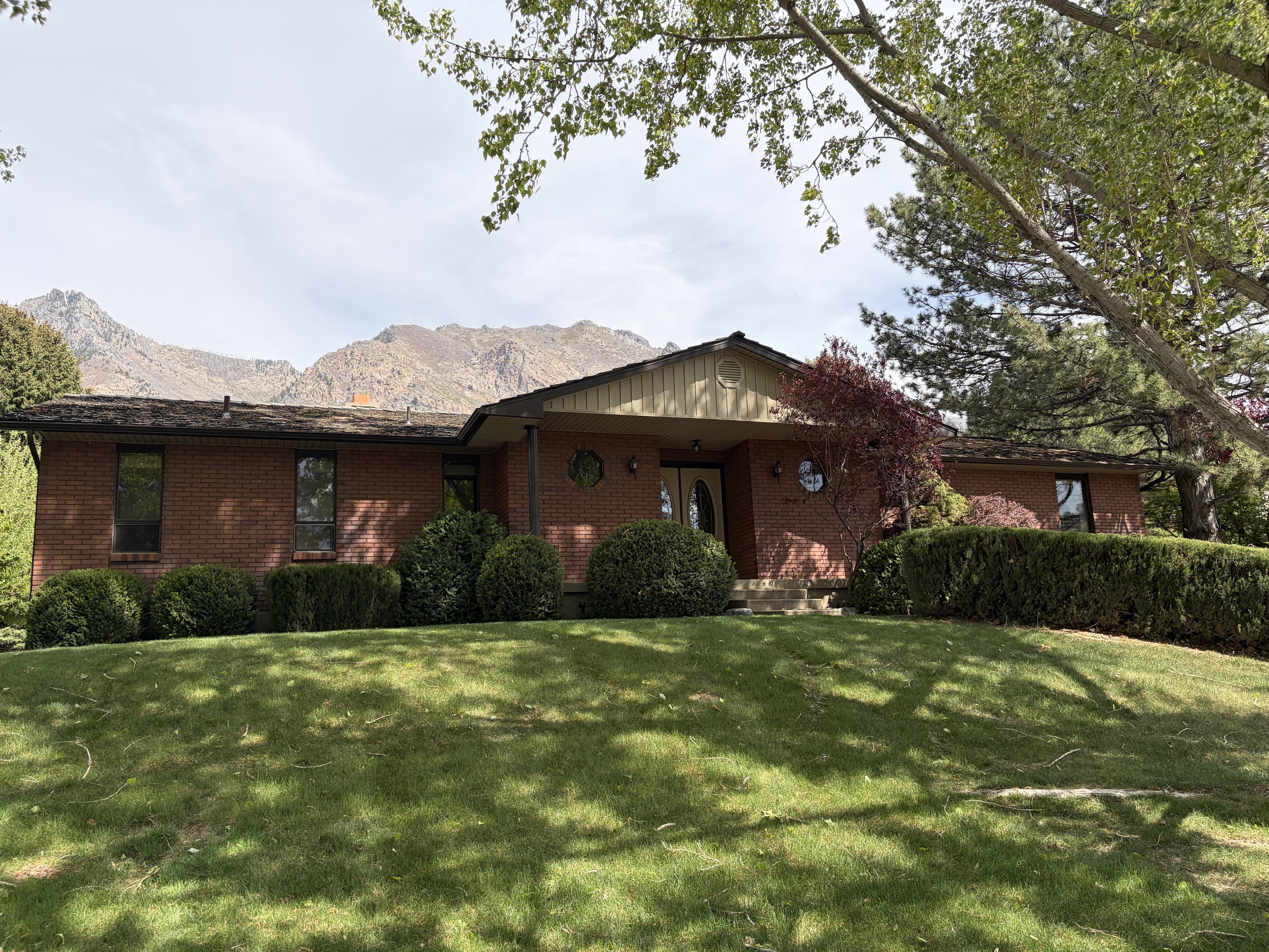 Ranch-style home featuring brick siding, a front lawn, covered porch, and a mountain view