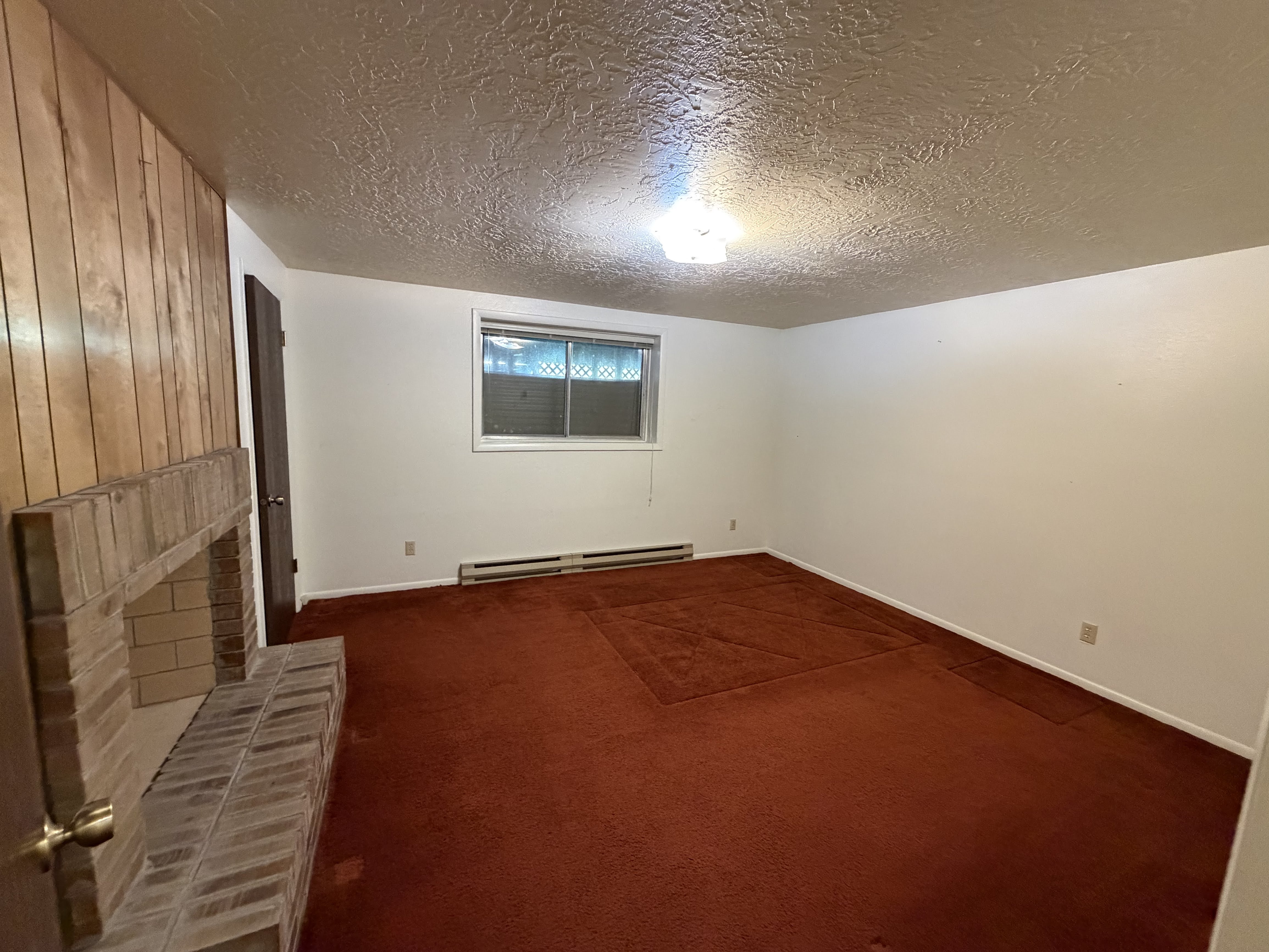 Empty room featuring dark colored carpet, a textured ceiling, and a baseboard heating unit