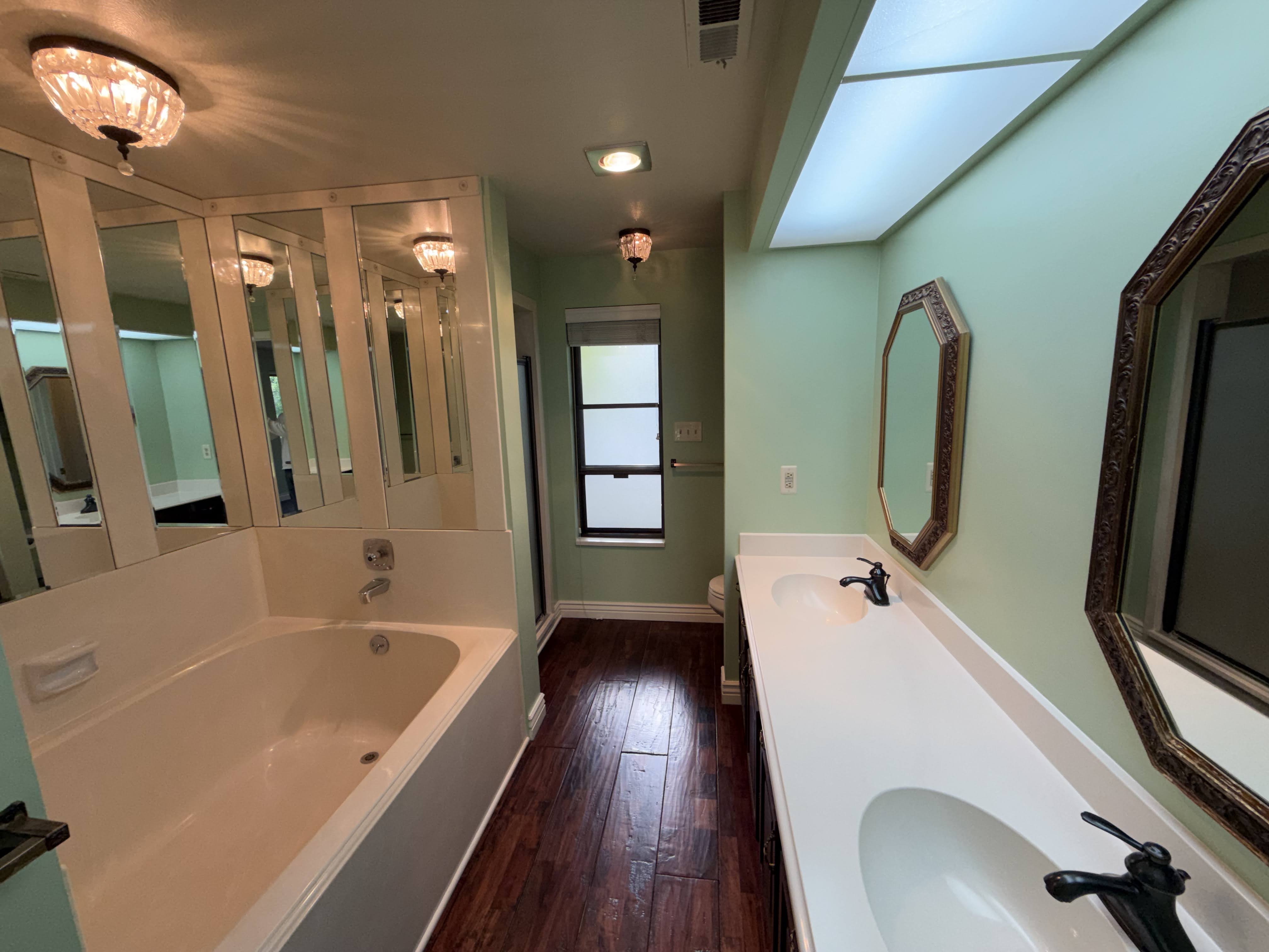 Full bathroom with double vanity, dark wood finished floors, and a garden tub