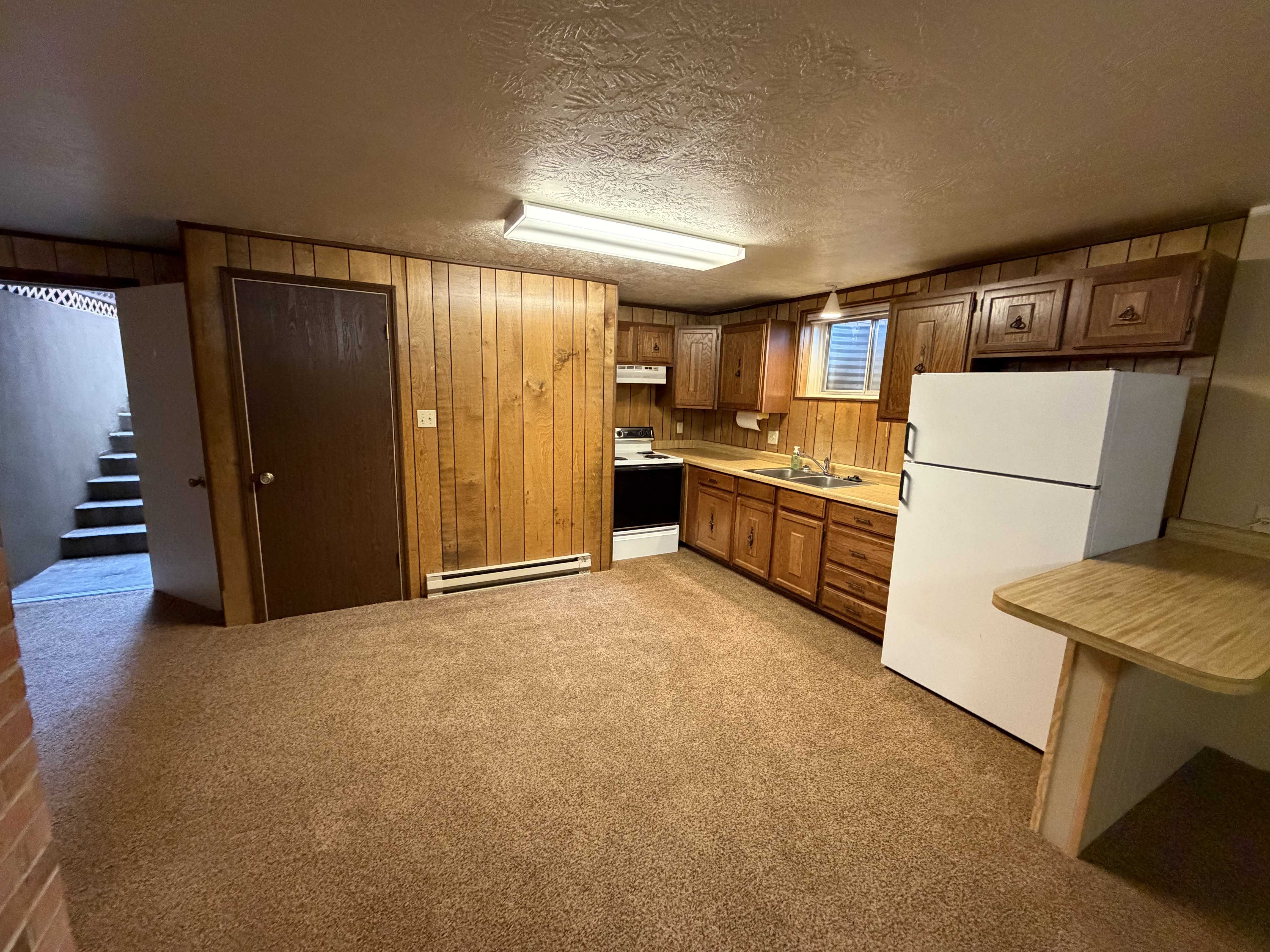 Kitchen with wood finish cabinetry, white appliances, light countertops, light colored carpet, and wood walls