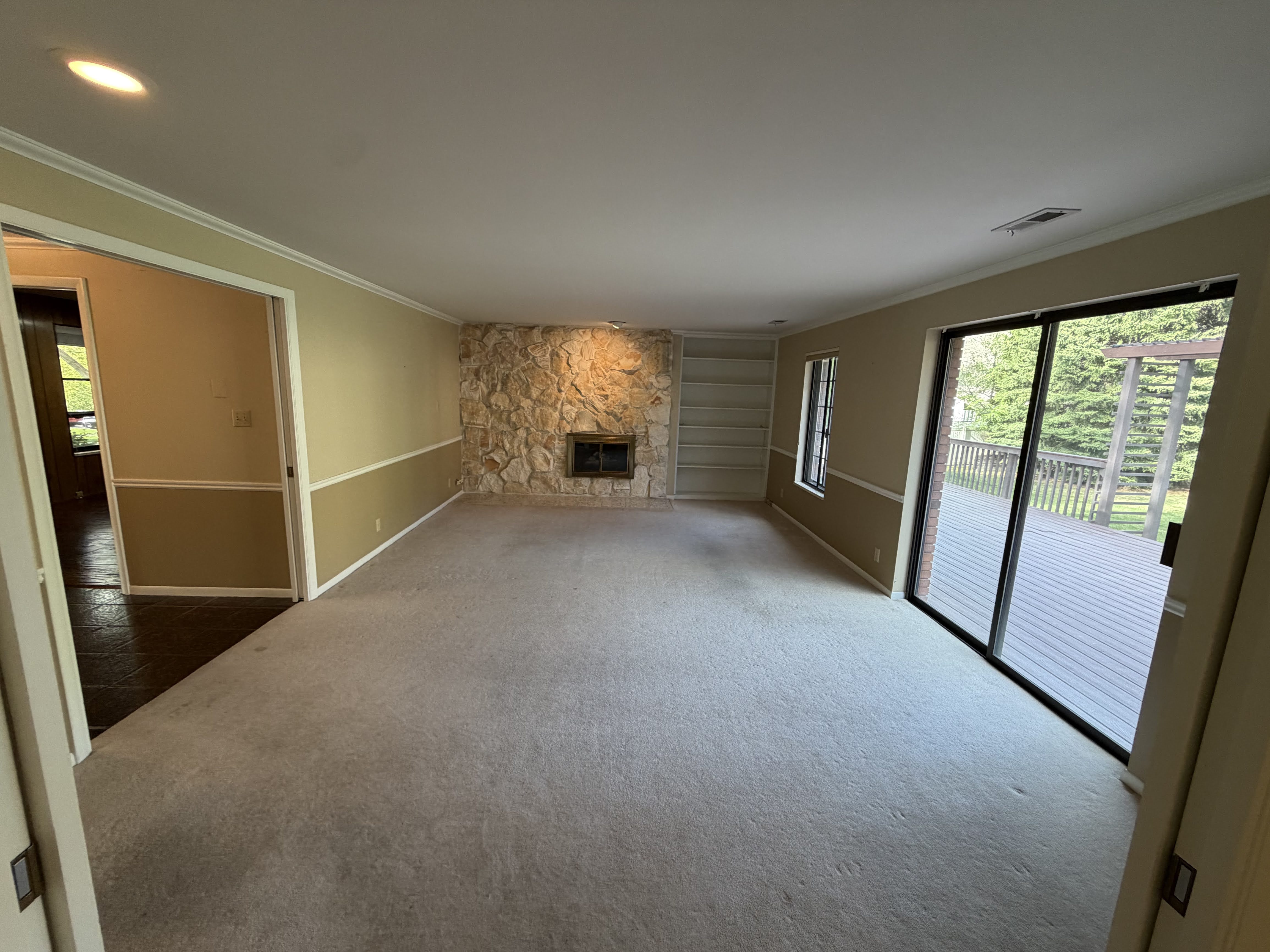 Unfurnished living room with a stone fireplace, ornamental molding, carpet floors, and recessed lighting