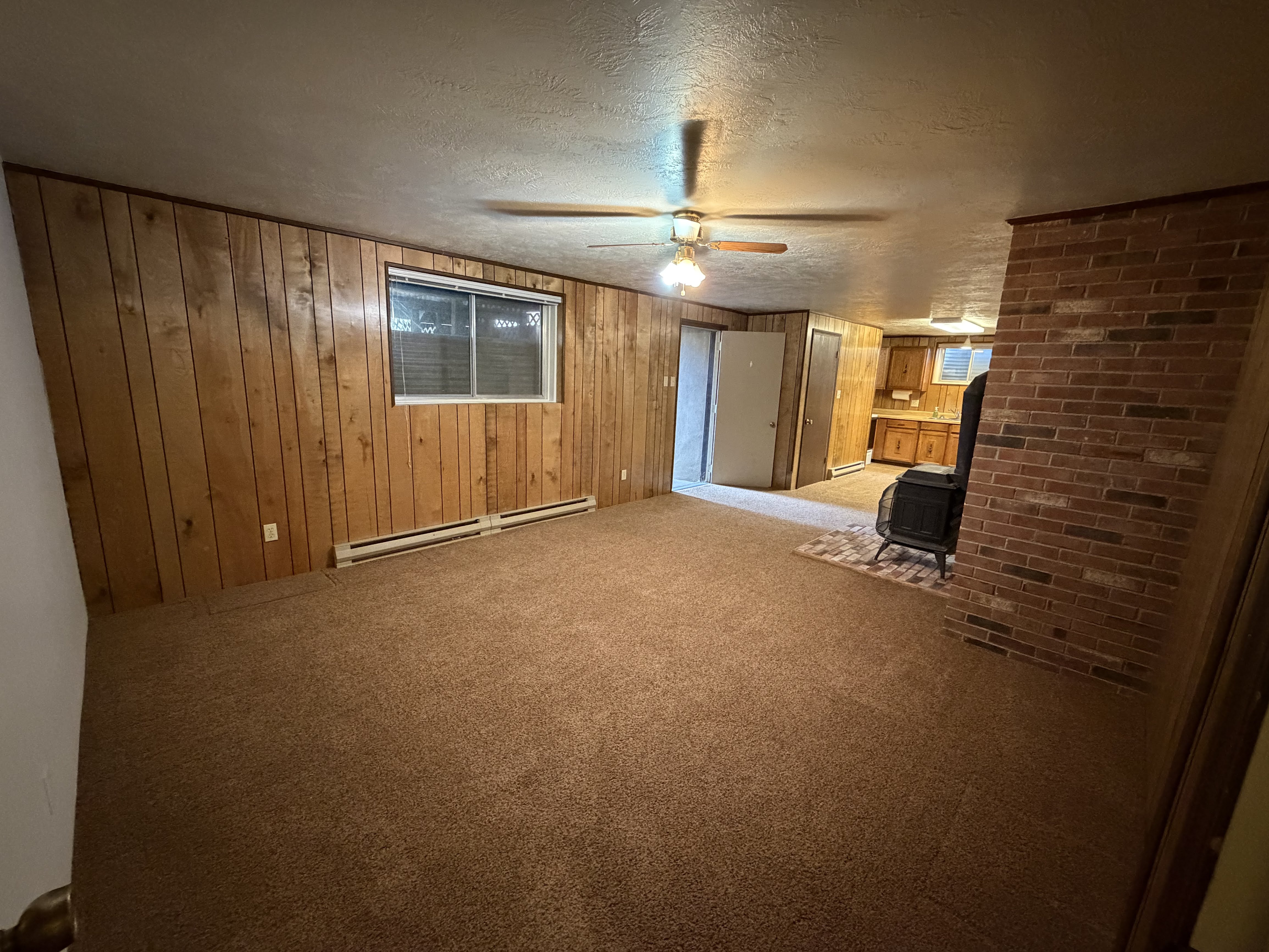Unfurnished living room with a wood stove, carpet, baseboard heating, wooden walls, and a textured ceiling