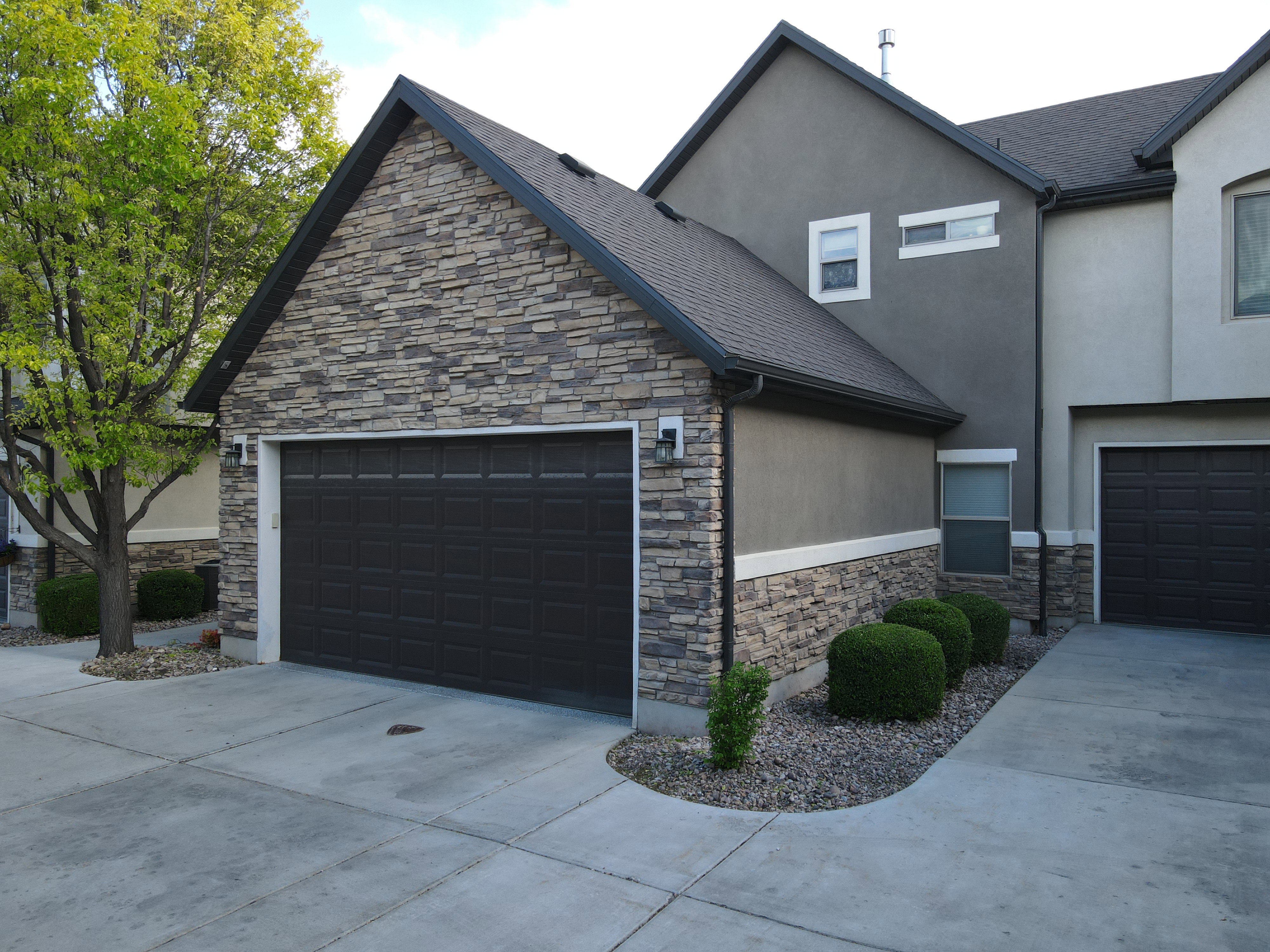 View of side of home with stone siding, stucco siding, driveway, and roof with shingles