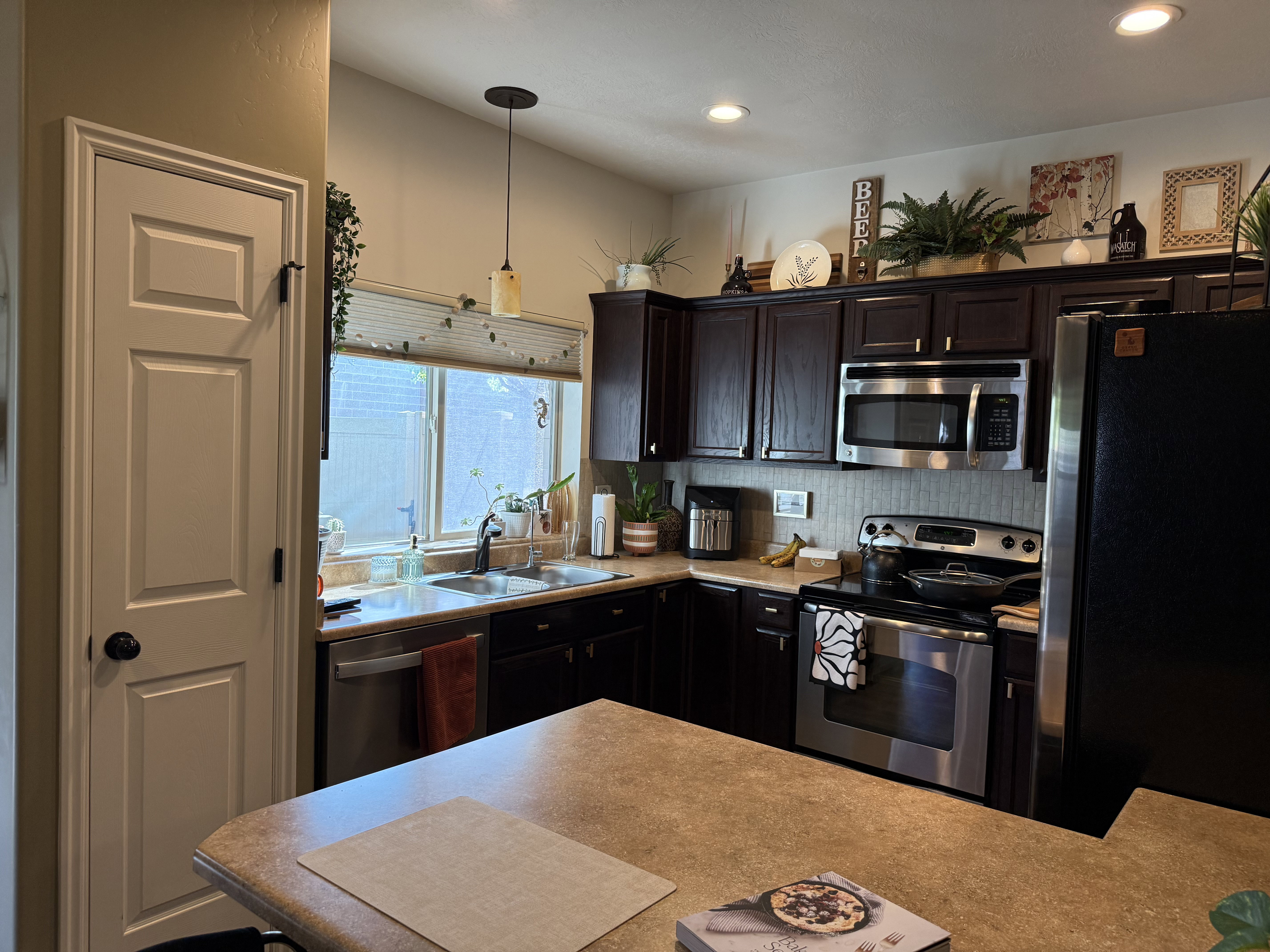 Kitchen featuring stainless steel appliances, light countertops, dark wood finish cabinetry, pendant lighting, and decorative backsplash