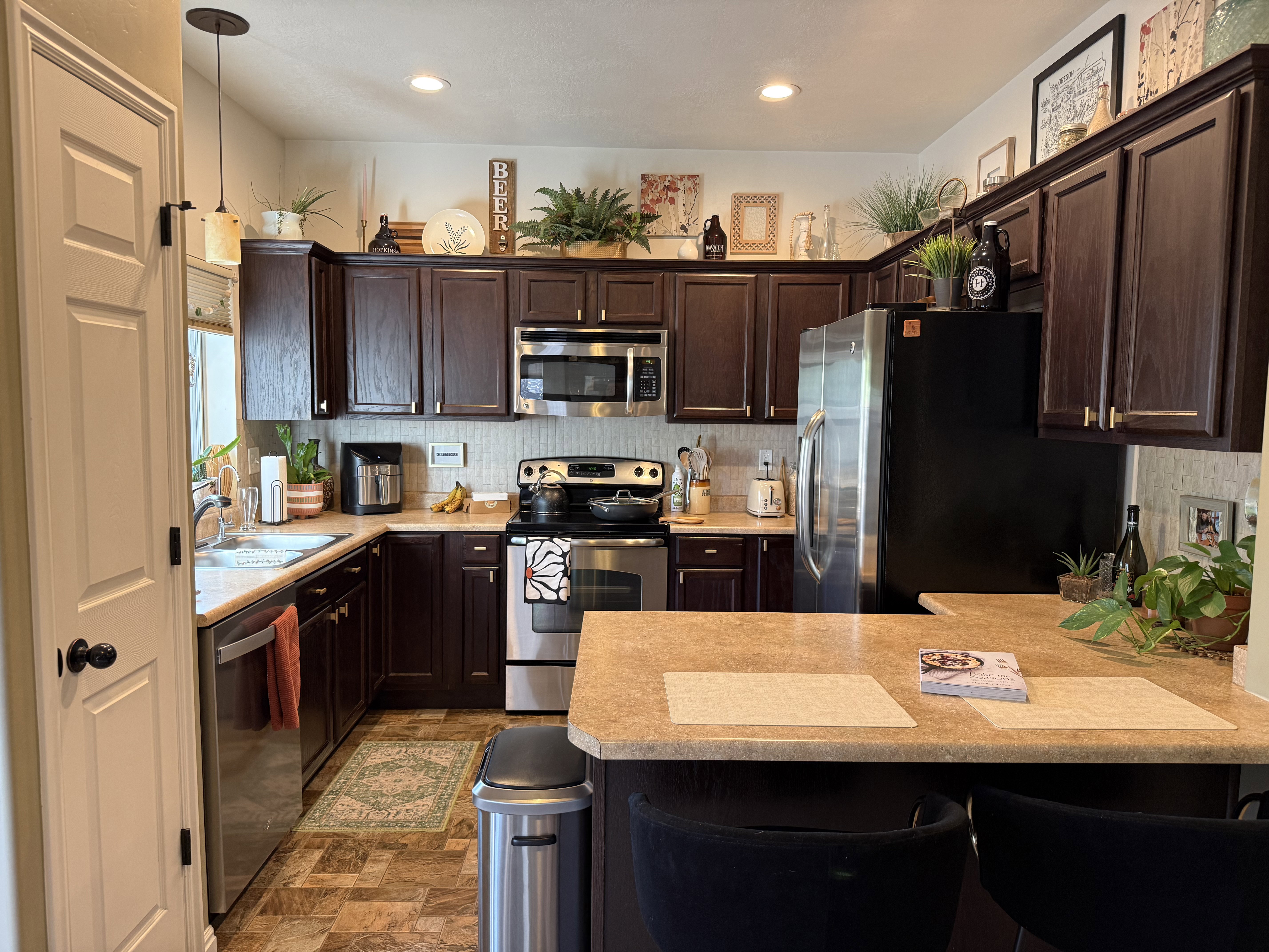 Kitchen with a peninsula, a kitchen breakfast bar, stainless steel appliances, dark wood finish cabinets, and light countertops