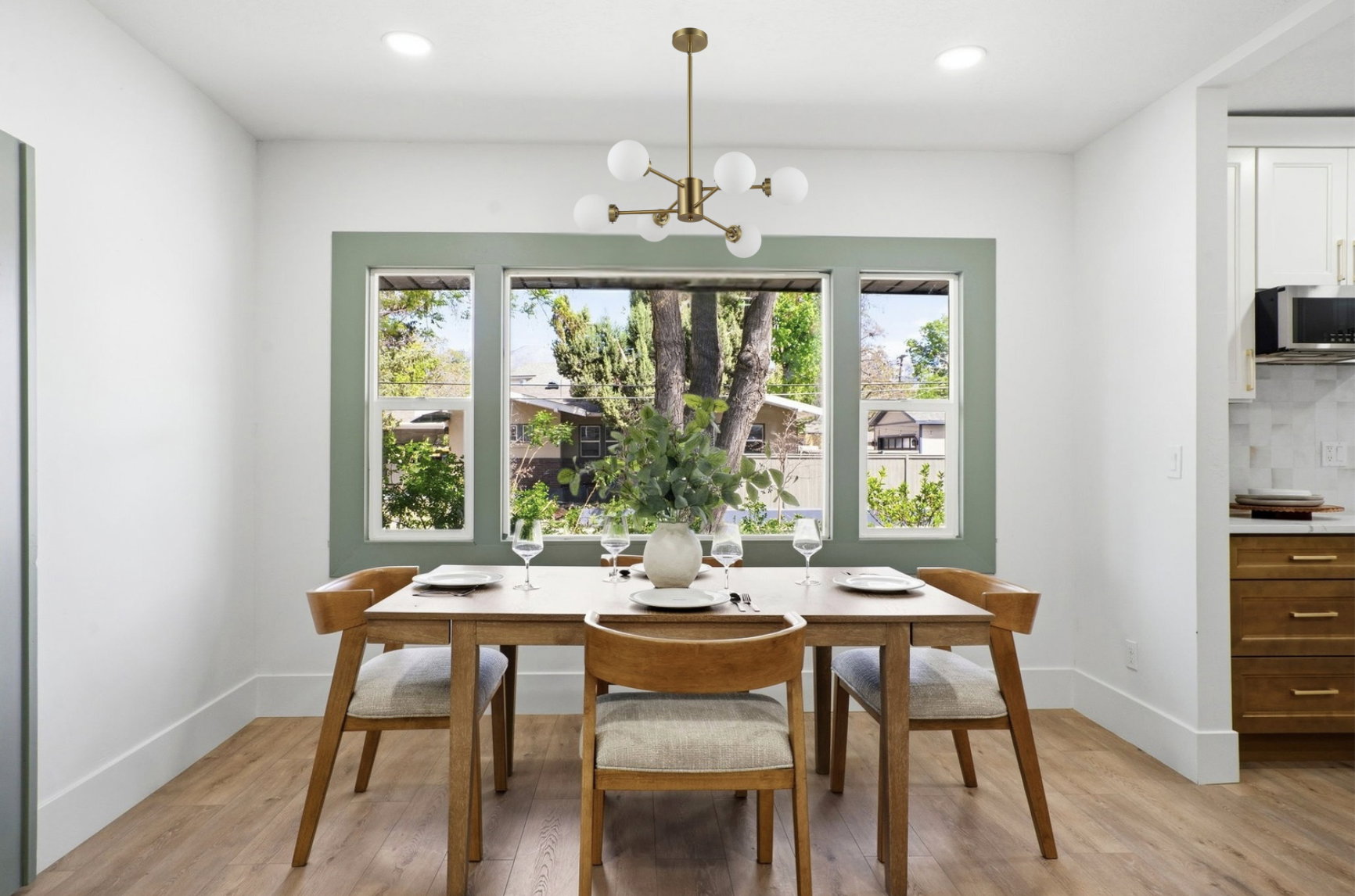 Bright dining area featuring a contemporary brass chandelier and expansive windows with green trim